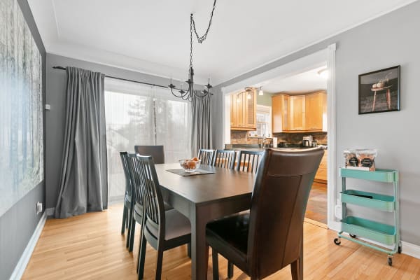 Modern dining room with a wooden table, glass bowl of oranges, and open kitchen view.