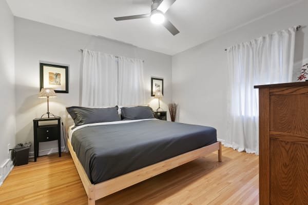 Cozy bedroom featuring a wooden bed with gray bedding, white curtains, and a decorative lamp.