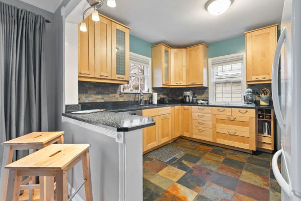 A contemporary kitchen with wooden cabinetry, granite countertops, and slate tile flooring.