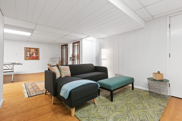 A living room with a black sectional sofa, colorful cushions, and a geometric rug on wooden flooring.