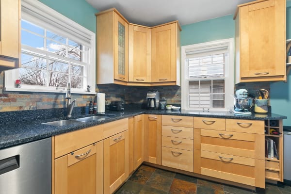 Contemporary kitchen with wooden cabinets, granite countertops, and a view through windows.