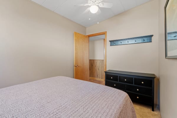Interior view of a cozy bedroom featuring a bed with a purple quilt, black dresser, and an open wooden door.