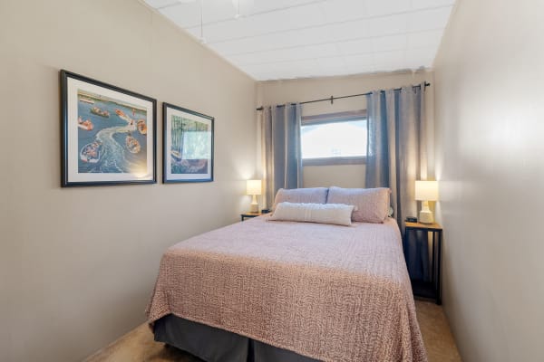 Inside a cozy bedroom featuring a bed, artwork on the walls, and soft lighting.