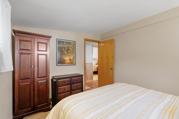 A warm-toned bedroom featuring a wooden wardrobe, dresser, and a white bed with yellow stripes.