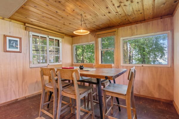 Cozy dining room with wooden furniture and large windows overlooking greenery.