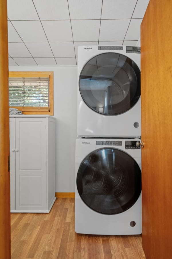 Compact laundry area with a stacked Whirlpool washer and dryer, white cabinet, and wooden flooring.