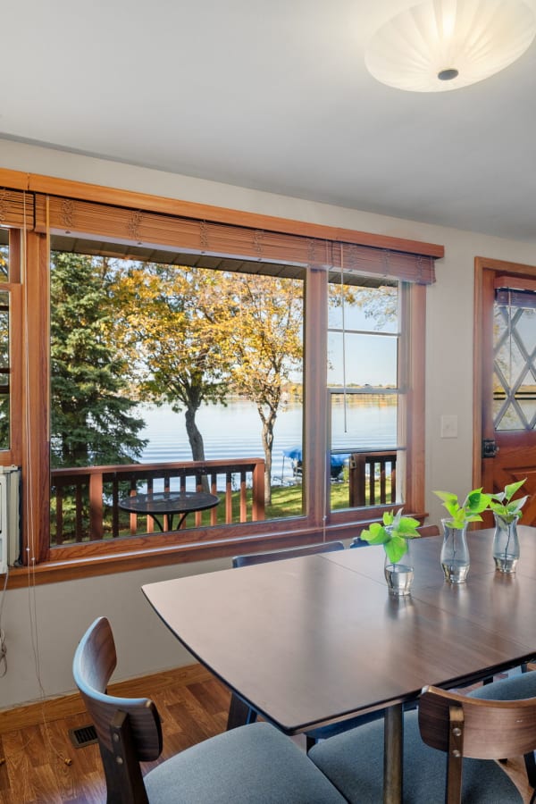 A bright dining room with large windows showcasing a lake and autumn trees.