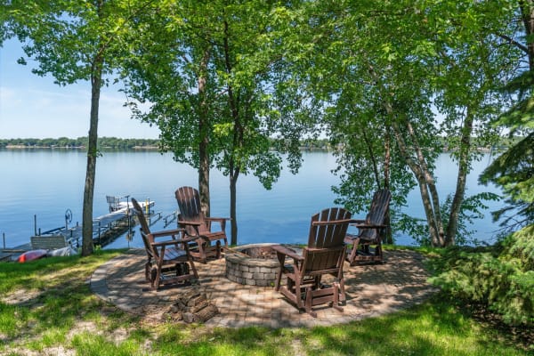 Lakeside fire pit area with Adirondack chairs and a dock in the background.