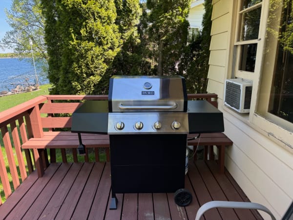 A black gas grill with stainless steel features on a wooden deck overlooking a lake.