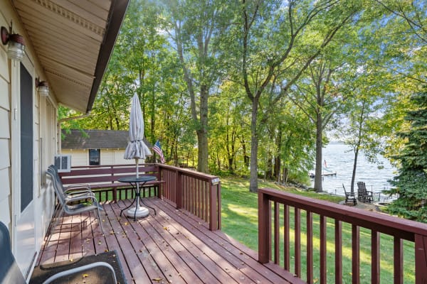 Wooden deck overlooking a lake surrounded by trees and grass.