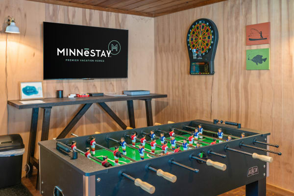 Indoor game room with foosball table, flat-screen TV, dartboard, and decorative wooden art.