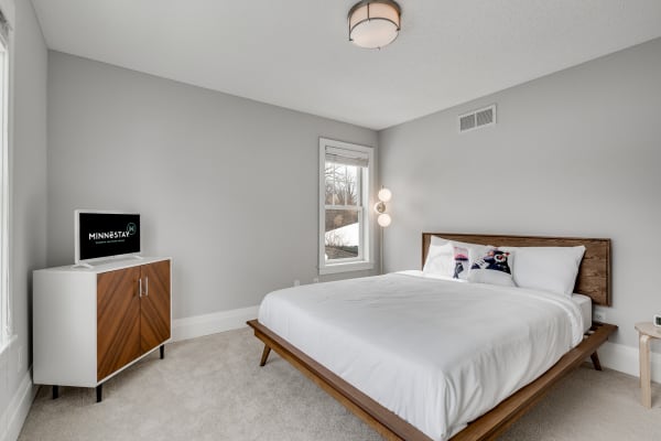 A modern bedroom with a wooden bed frame, white bedding, and a flat-screen TV on a cabinet.