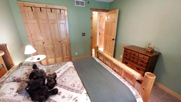 A rustic styled bedroom featuring a log bed, floral quilt, and stuffed toy moose.