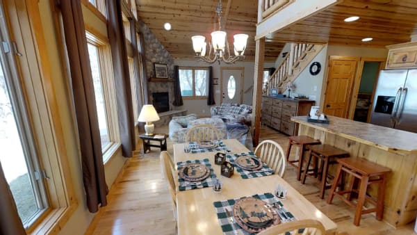 Interior view of a cozy cabin with dining table, living area, and large windows.