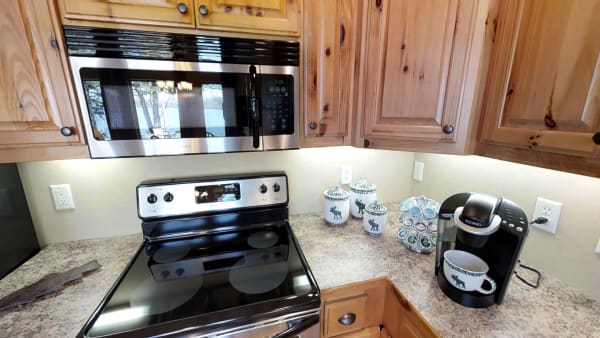 Kitchen with wooden cabinets, black glass-top stove, microwave, and coffee maker, set against a peaceful background of trees and water.