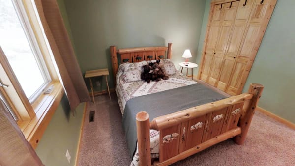 A bedroom featuring a log bed, patchwork quilt, and carved headboard with animals.