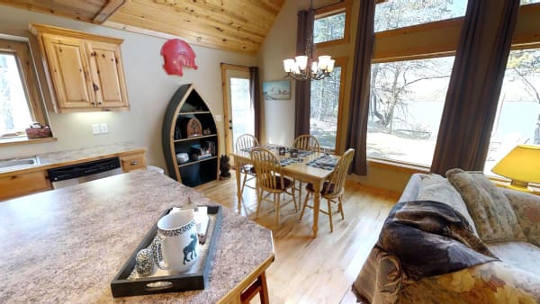 Interior of a lakeside cabin with a dining area, large windows, and a cozy sofa.