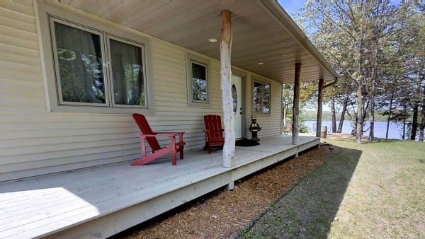 Cottage porch with red chairs overlooking a lake, surrounded by trees.
