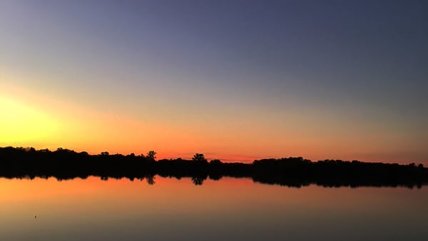 A stunning sunset over a lake with reflections in the water and silhouetted trees.