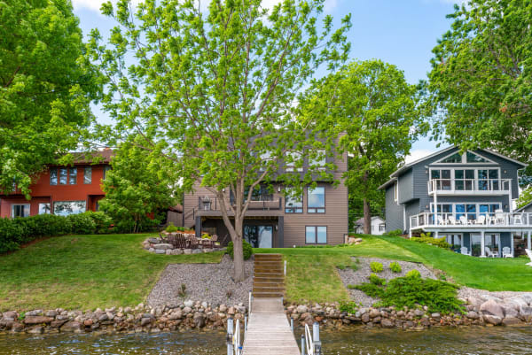 A lakeside view featuring three houses with greenery and a wooden dock.