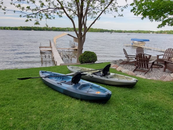Two kayaks on grass near a lake with a wooden dock.