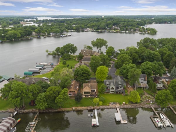 Aerial view of residential homes along a lakeside surrounded by trees.