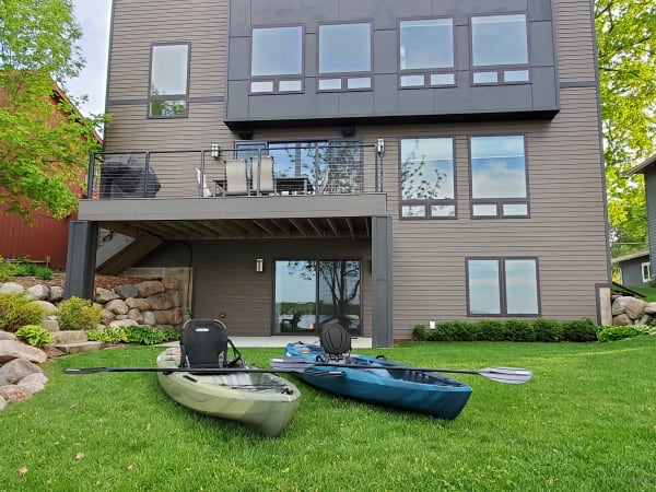 A modern home with large windows by the lake, featuring kayaks on the lawn.