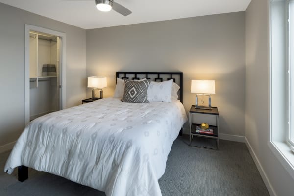 Interior view of a stylish bedroom featuring a bed with a white quilt and decorative pillows, nightstands with lamps, and a window.