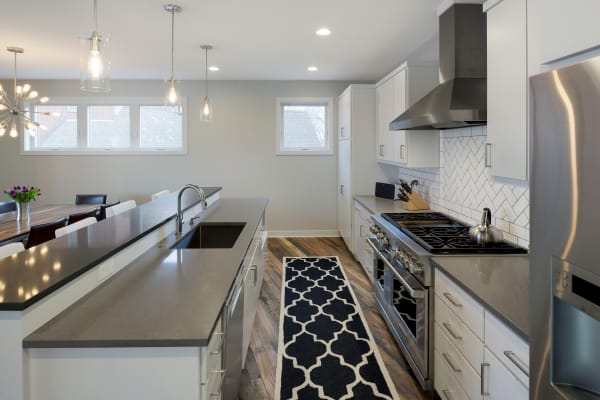 Modern kitchen with white cabinets, a countertop, and wood flooring, featuring a dining area in the background.
