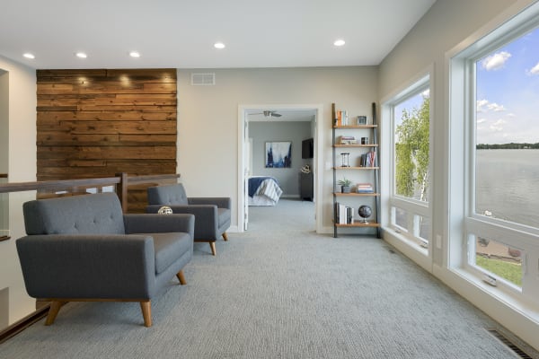 Modern living space featuring gray chairs, wood accent wall, bookshelf, and lake view.
