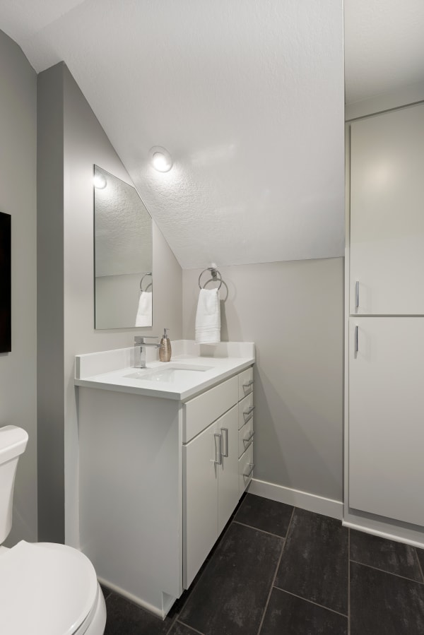 Modern bathroom with gray walls, white vanity, and dark tile flooring.