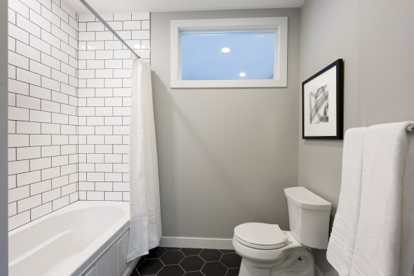 Modern bathroom featuring a white bathtub, subway tiles, gray walls, and hexagonal black tiles.