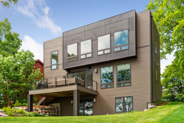Contemporary house with large windows, wooden siding, and a deck surrounded by greenery.