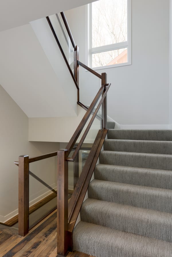 A contemporary staircase with a wooden bannister and gray carpet.