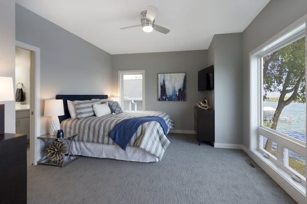 Modern bedroom with gray walls, a double bed, and large windows overlooking a lake.