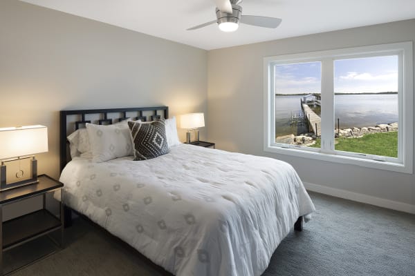 A serene bedroom featuring a bed, bedside tables, and a large window overlooking a tranquil lake and dock.