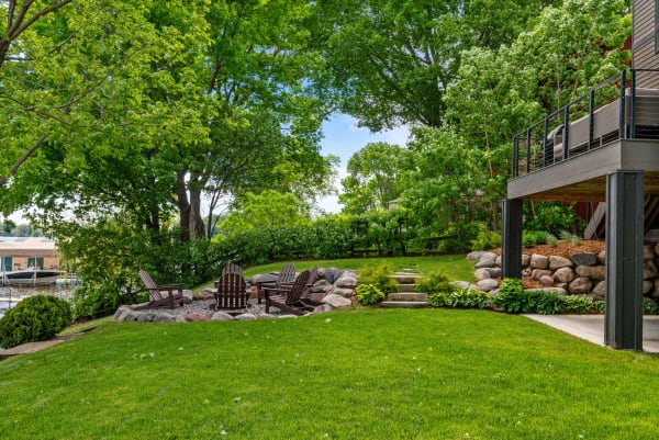 Backyard with fire pit and Adirondack chairs, surrounded by trees and a modern deck.