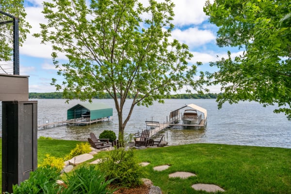 Lakeside view featuring a tree, docks with boats, and green grass seating area.
