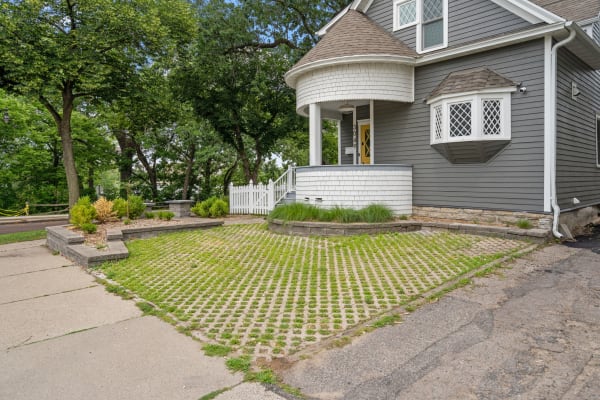 A gray house with a round porch, yellow door, and landscaped yard featuring paver stones and greenery.