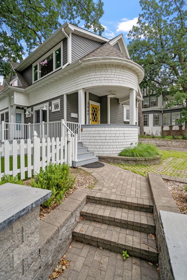 Charming two-story house with a round porch, gray siding, and yellow door.