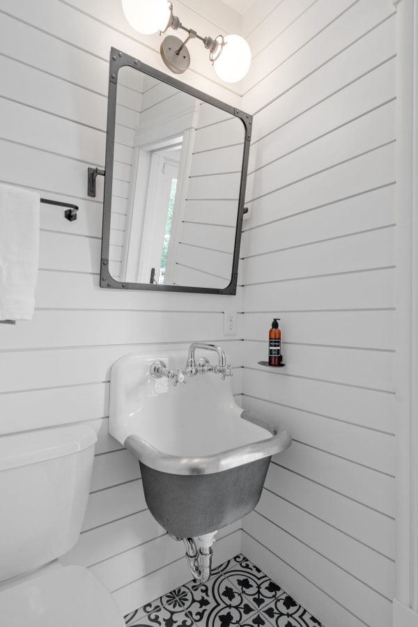 Modern small bathroom with white shiplap walls, vintage-style sink, and patterned floor tiles.
