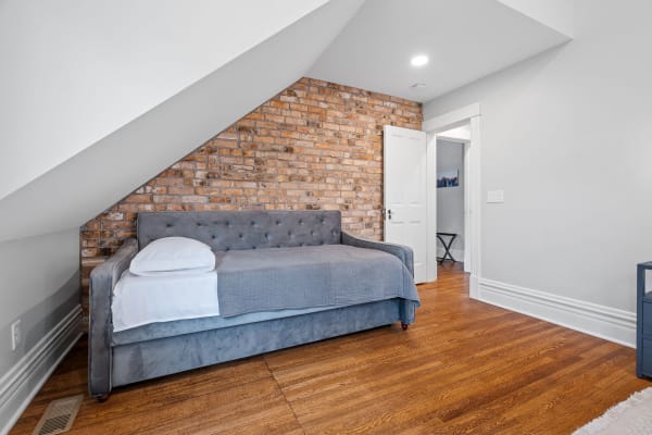 Cozy attic bedroom with gray daybed and exposed brick wall.