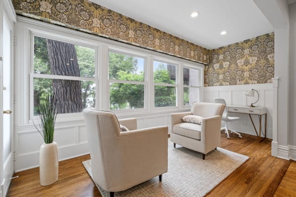 A bright sitting area featuring two armchairs, patterned wallpaper, and a small desk with a lamp.