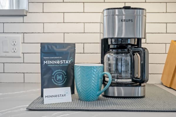 A KRUPS coffee maker next to a turquoise herringbone mug and a coffee bag from MINNESTAY.