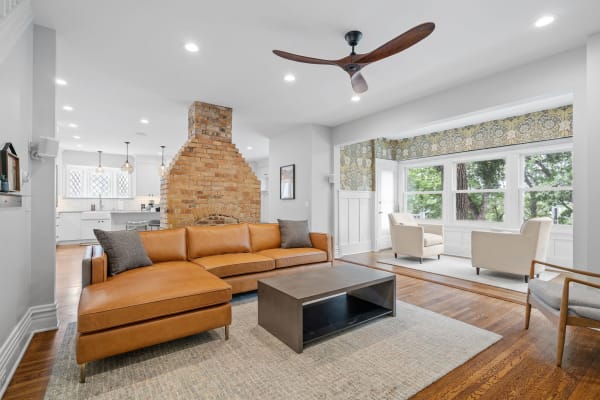 Cozy living room with a leather sectional, coffee table, and large windows overlooking greenery.