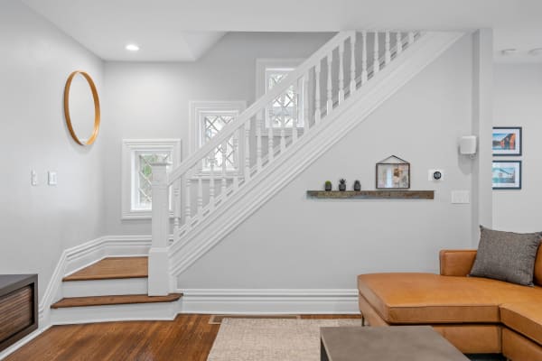 A stylish living area featuring a staircase, round mirror, and potted plants on a shelf.