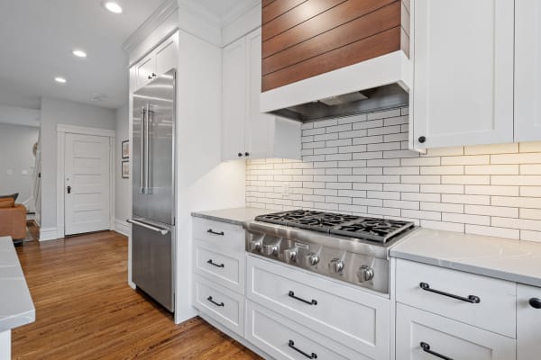 Interior view of a modern kitchen with a gas range, stainless steel refrigerator, and white cabinetry.