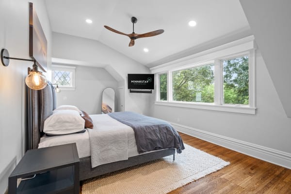 A modern bedroom featuring a large bed, cozy decor, and bright windows with greenery outside.