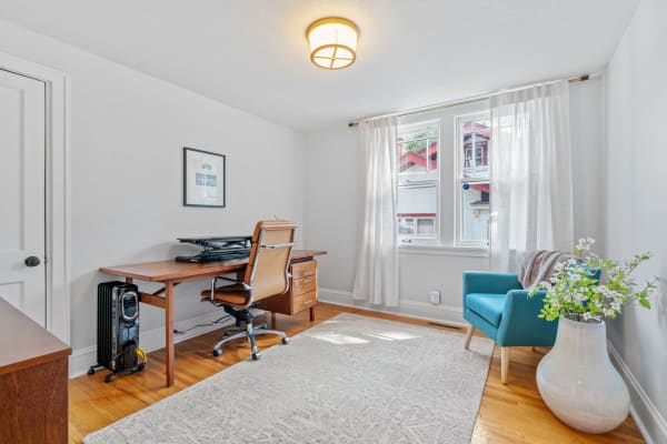 Home office featuring a desk, chair, and turquoise armchair with a vase of flowers.