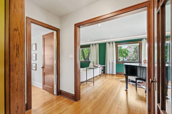 A hallway leading into a room with green walls, a grand piano, and natural light coming through large windows.